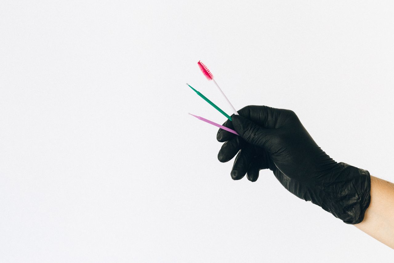 A black glove holds colorful dental brushes against a white backdrop.